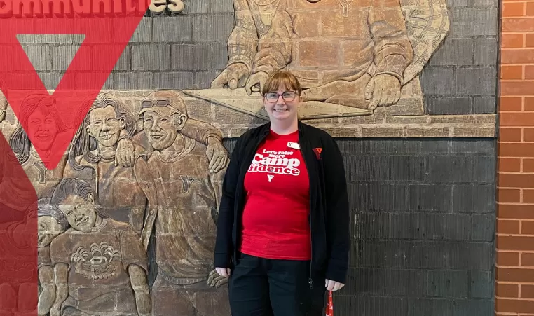 Jenn Egan poses in front of a mural at Shawnessy YMCA with a smile on her face, donning YMCA clothing
