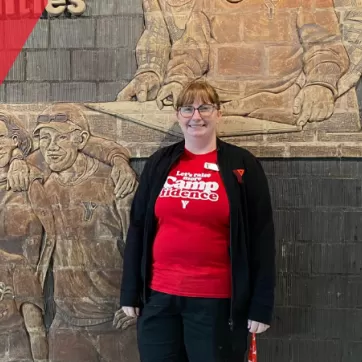 Jenn Egan poses in front of a mural at Shawnessy YMCA with a smile on her face, donning YMCA clothing
