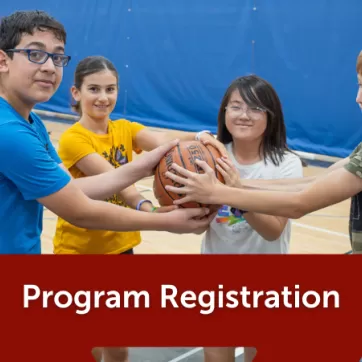 4 youth hold onto a basketball together, smiling and enjoying their time at the YMCA. The header says Program Registration on a dark red triangle graphic.