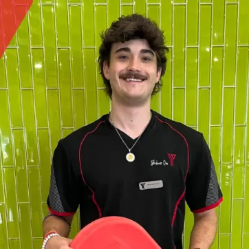 Wesley, the lifeguard, stands in front of a green wall with a smile on his face